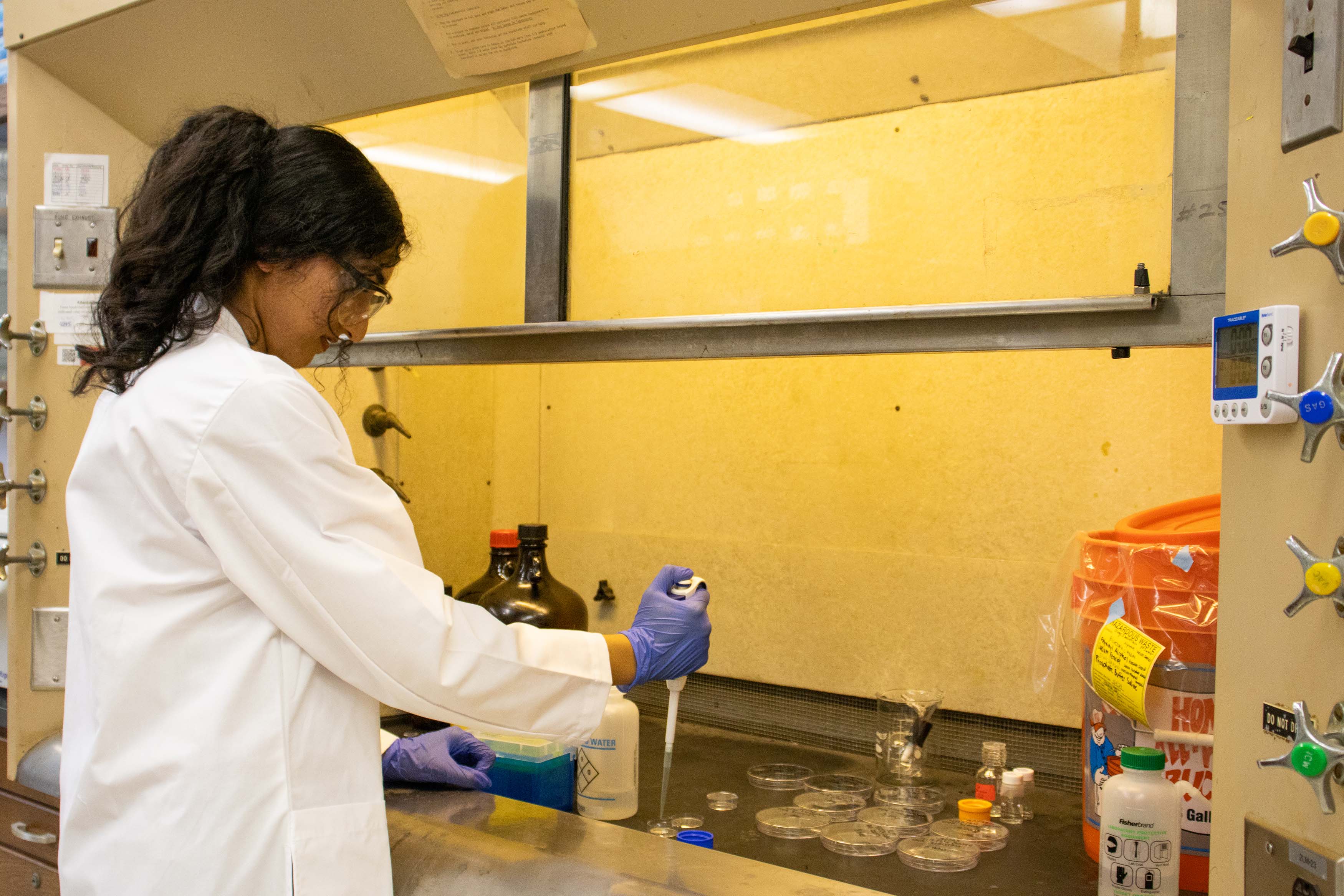 female research student in white coat standing in lab using an autopipette
