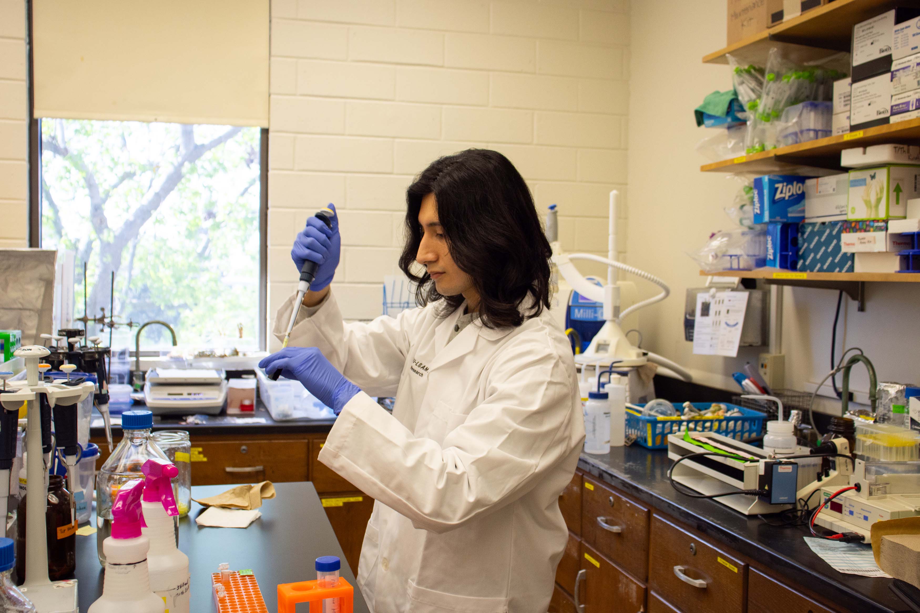 male research student in white coat standing in lab using an autopipette