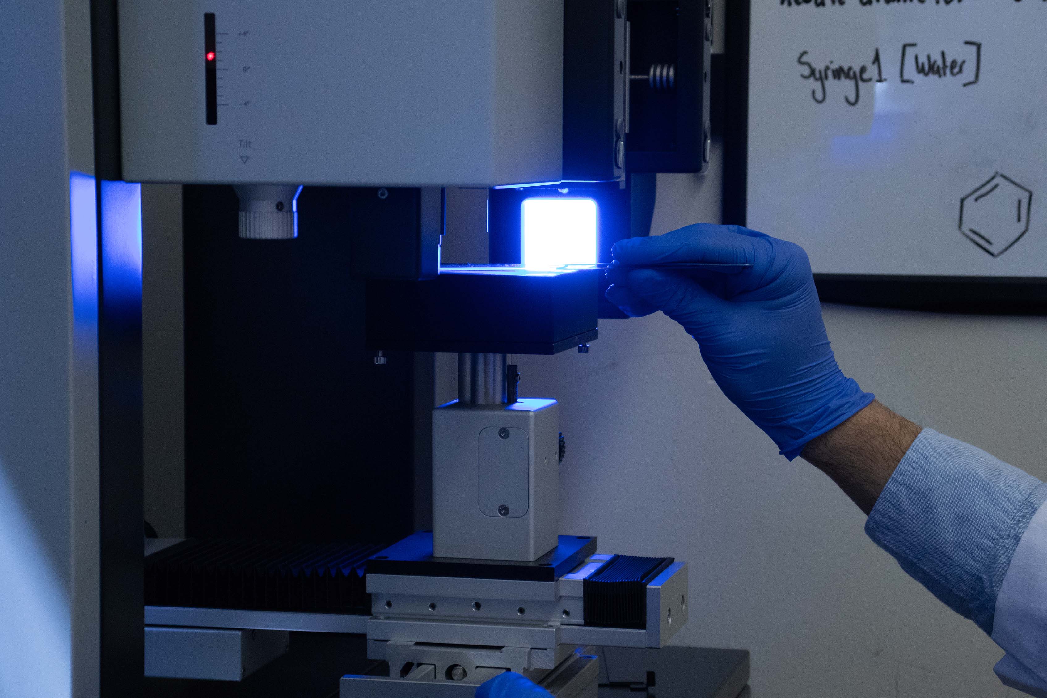 Image of hand placing a glass slide onto an instrument with a bright blue/white light.