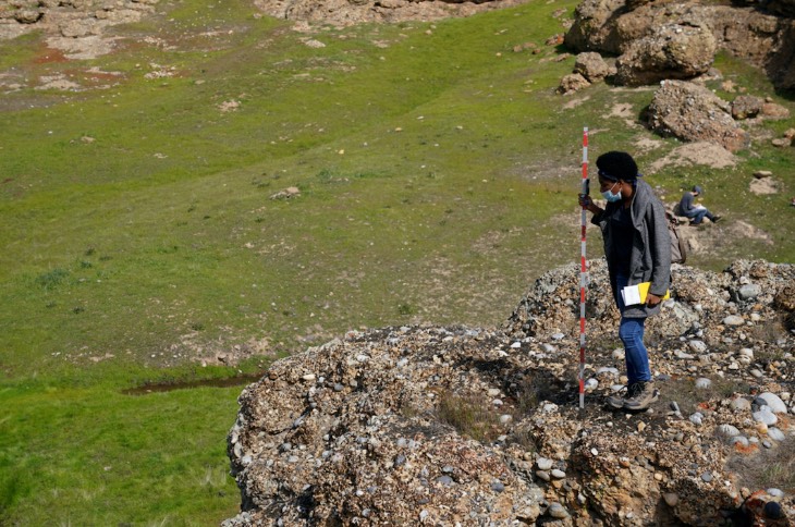 Geology student in the field; they are holding a Jacob's staff and overlooking rock formations