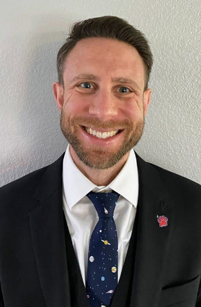 Male smiling at the camera wearing a suite and tie