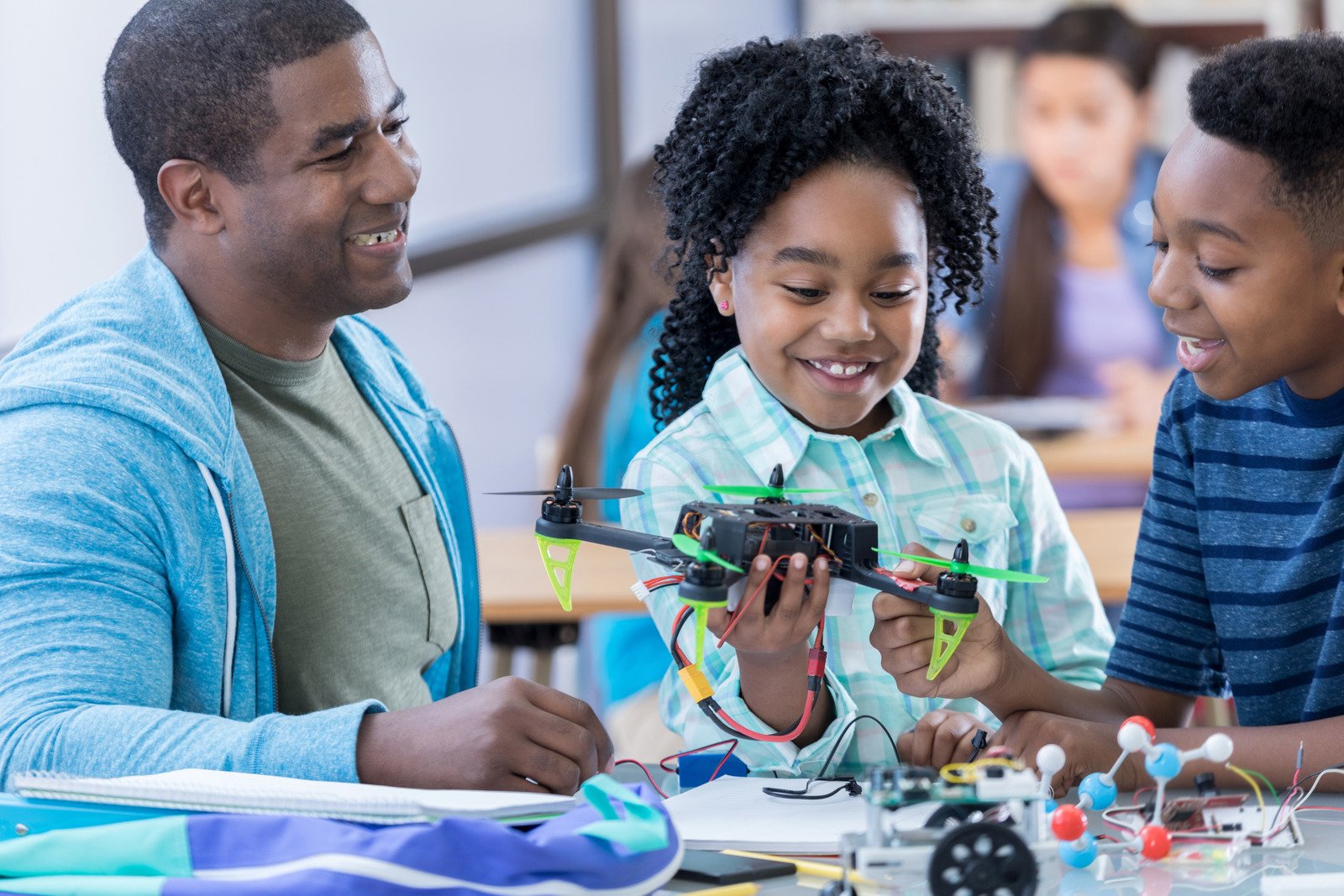 Man with 2 kids smiling, children are holding a small drone