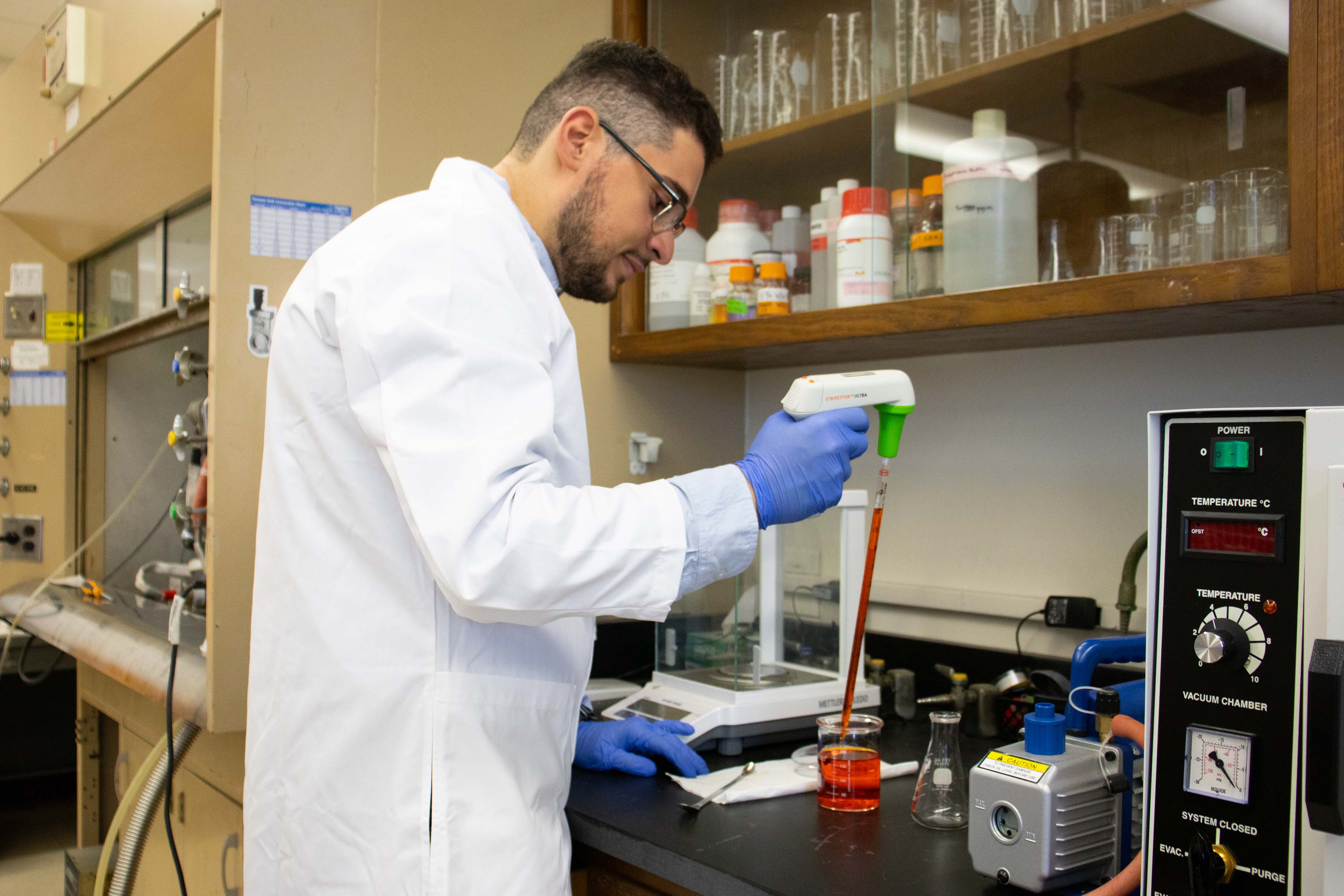 male research student in white coat standing in lab using a pipette