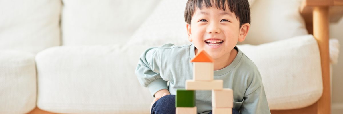 Young Child Playing A child looking at the camera and smiling with a stack of toy blocks assembled into a tower.