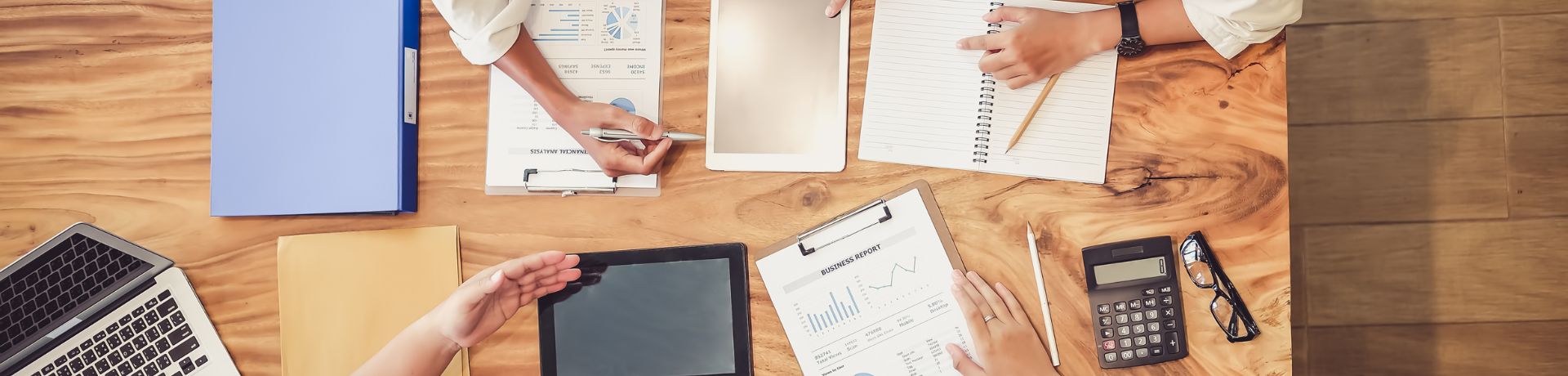 Hard at Work A desk with notebooks, clipboards, paper, calculators, and other work-related materials strewn about with people's hands manipulating the materials.