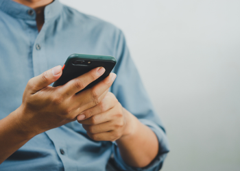 View of a person's hands holding a cell phone, with the phone oriented towards the person's face that is not pictured.
